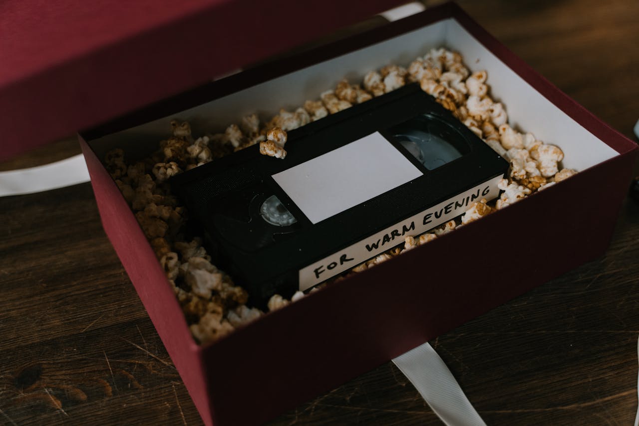 get-in-touch A nostalgic VHS tape resting in a popcorn-filled gift box on a wooden surface, perfect for a cozy movie night.